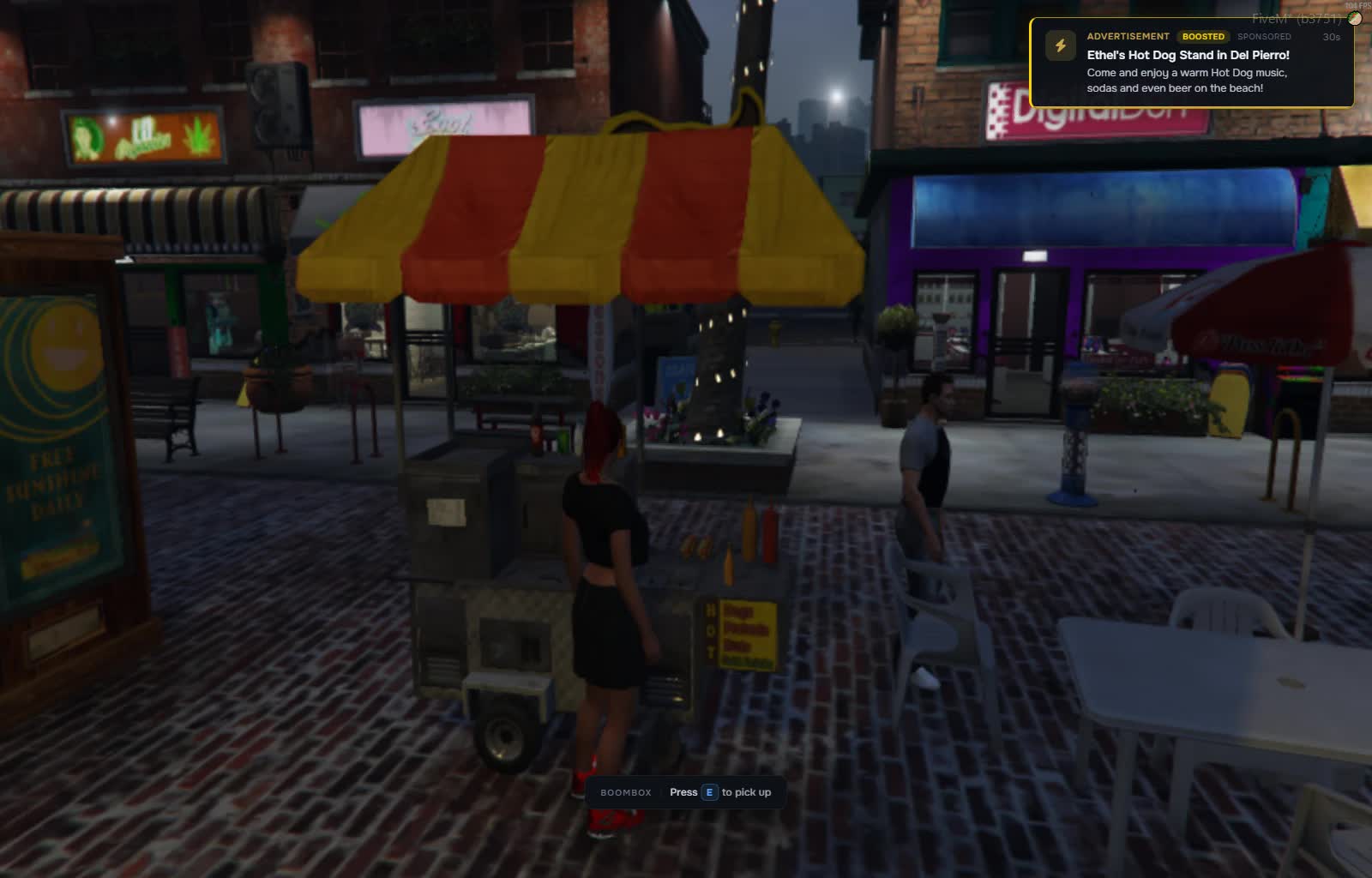A player-run hot dog stand on a plaza at night with an in-game advert on screen
