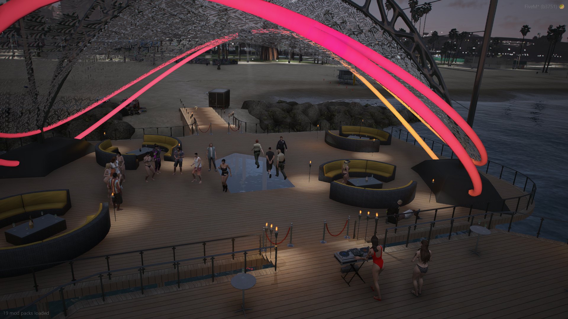 A wide view of the festival deck at dusk, neon arches overhead and the beach behind
